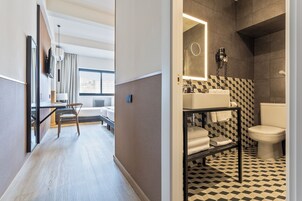 Una camera d'albergo moderna con pavimento in legno, un letto, una scrivania con sedia, una TV a parete e un'ampia finestra.