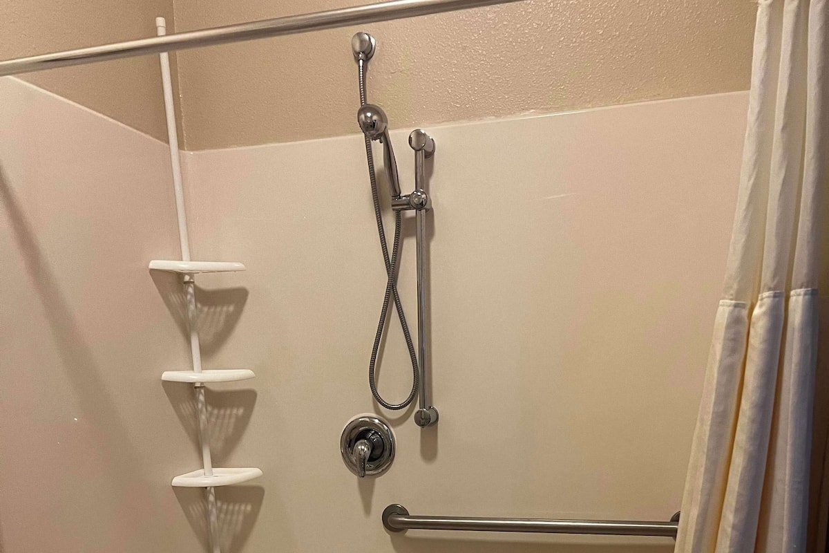 A walk-in shower with a grab bar, a white bench, and a showerhead.