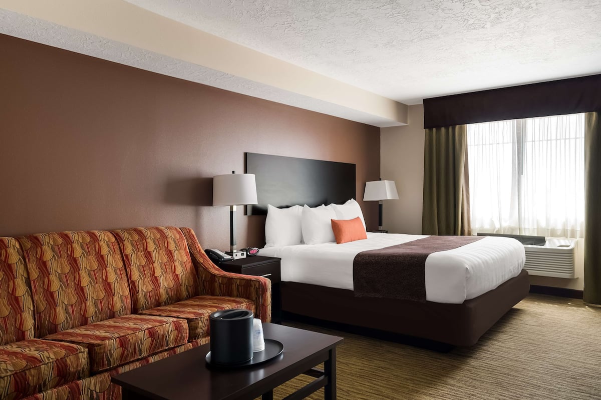 A hotel room with a bed, a sofa, a nightstand, a lamp, and a coffee maker.