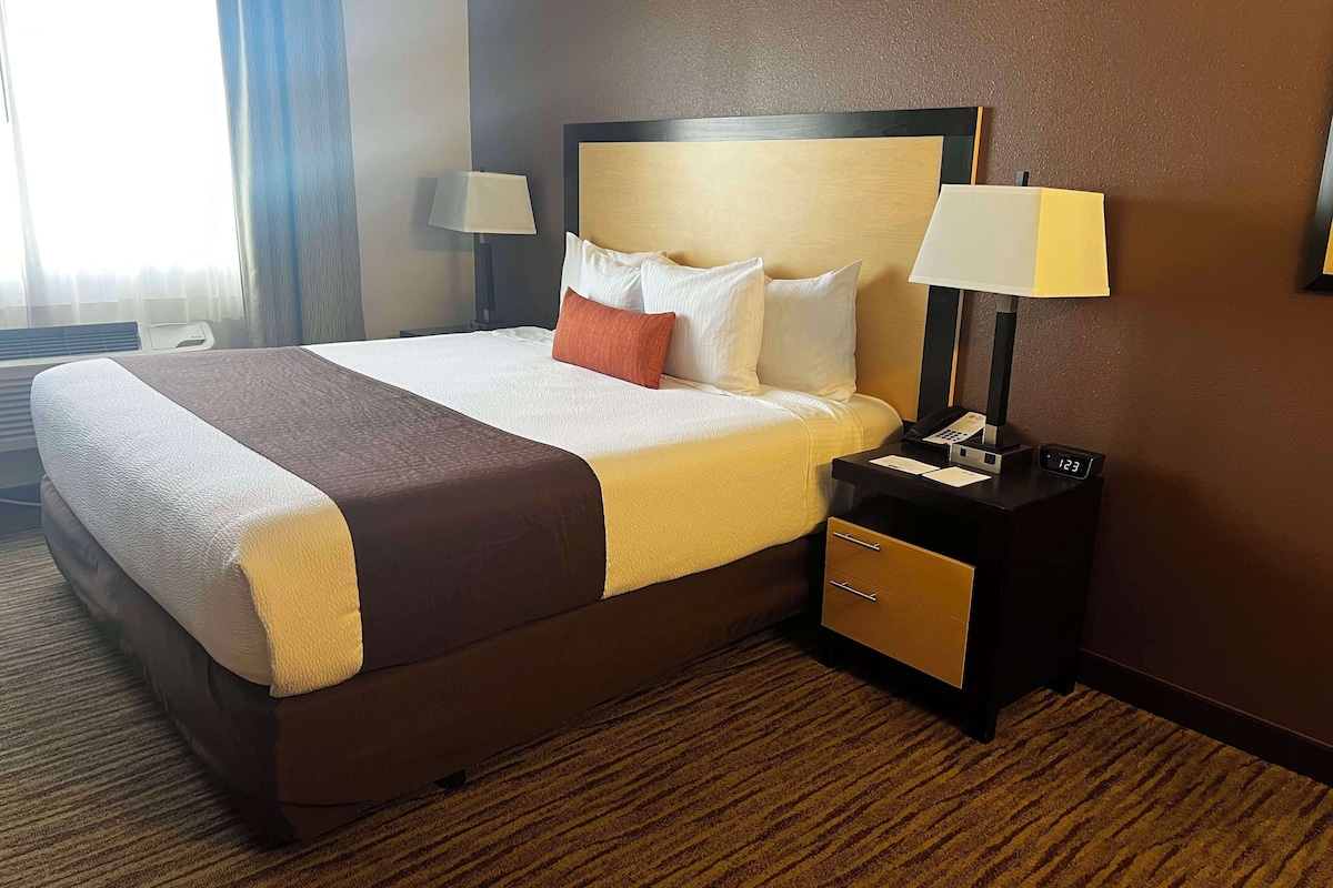 A hotel room with a large bed, two bedside tables, a nightstand, and a wall-mounted clock.