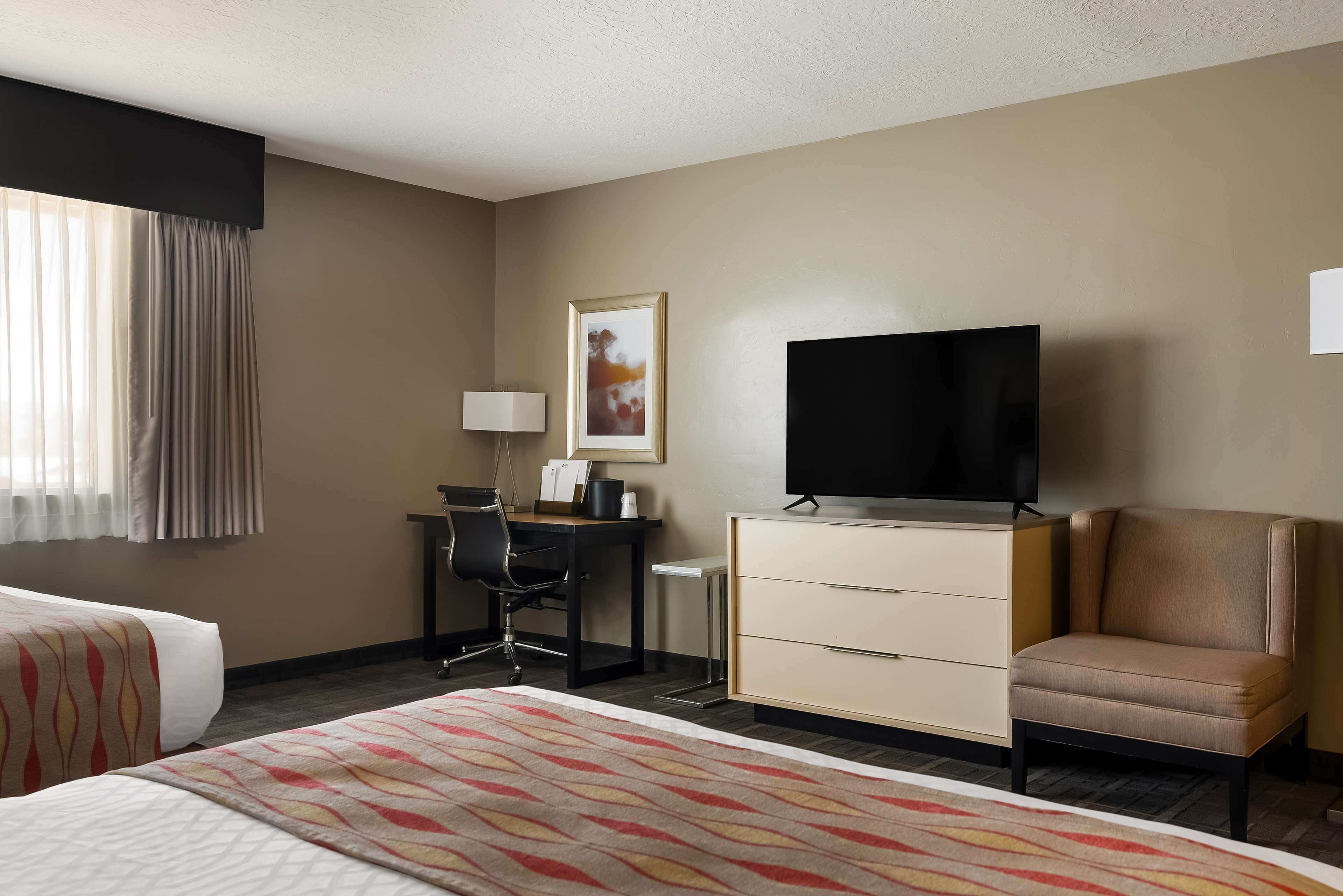 A hotel room with a bed, a desk, a television, a chair, and a dresser.