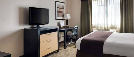 A hotel room with a bed, a desk with a computer, a television, and a window with curtains.