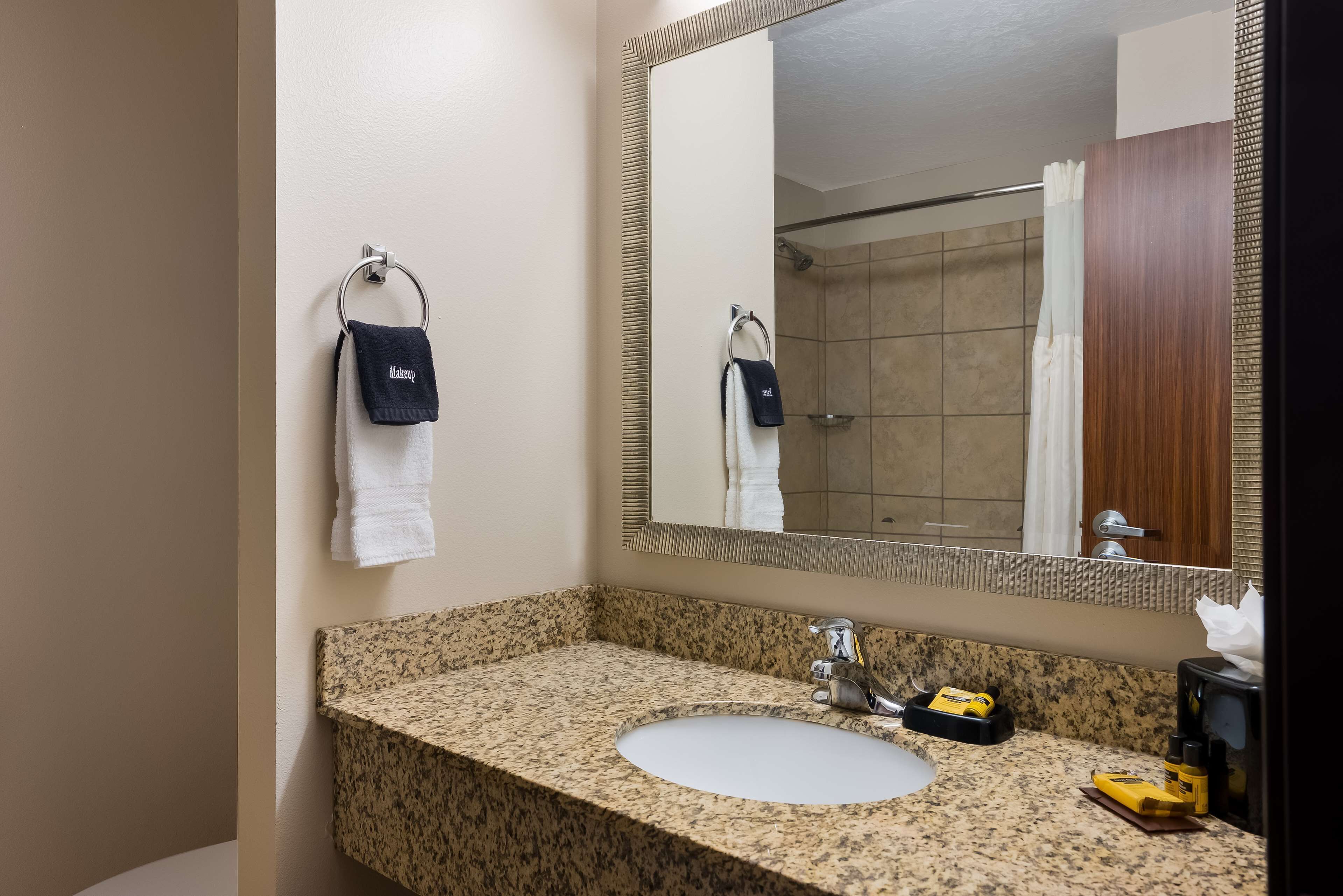 Un baño con lavamanos de granito, un espejo y dos toallas colgadas en la pared.