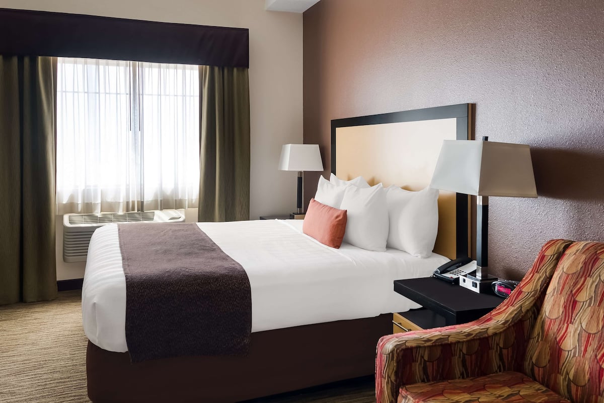A hotel room with a large bed, two bedside lamps, a telephone, and a chair.