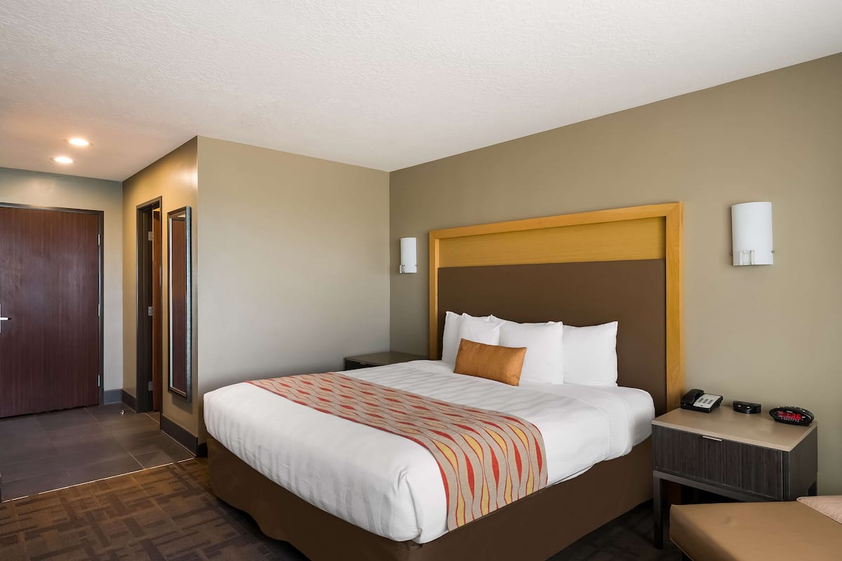 A hotel room with a large bed, a nightstand with a phone and a radio, and a door to the left.