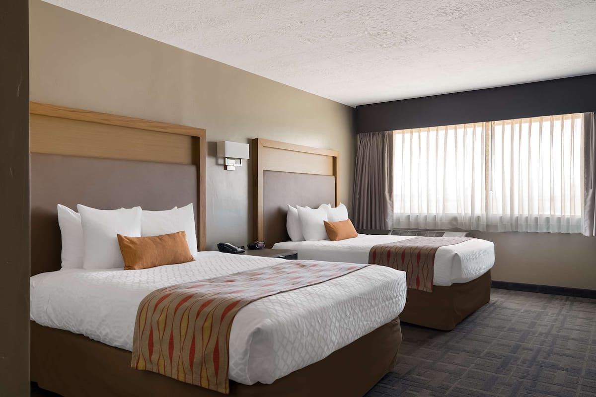 A hotel room with two beds, a large window with curtains, and a wall-mounted phone.