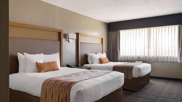 A hotel room with two beds, a large window with curtains, and a wall-mounted phone.