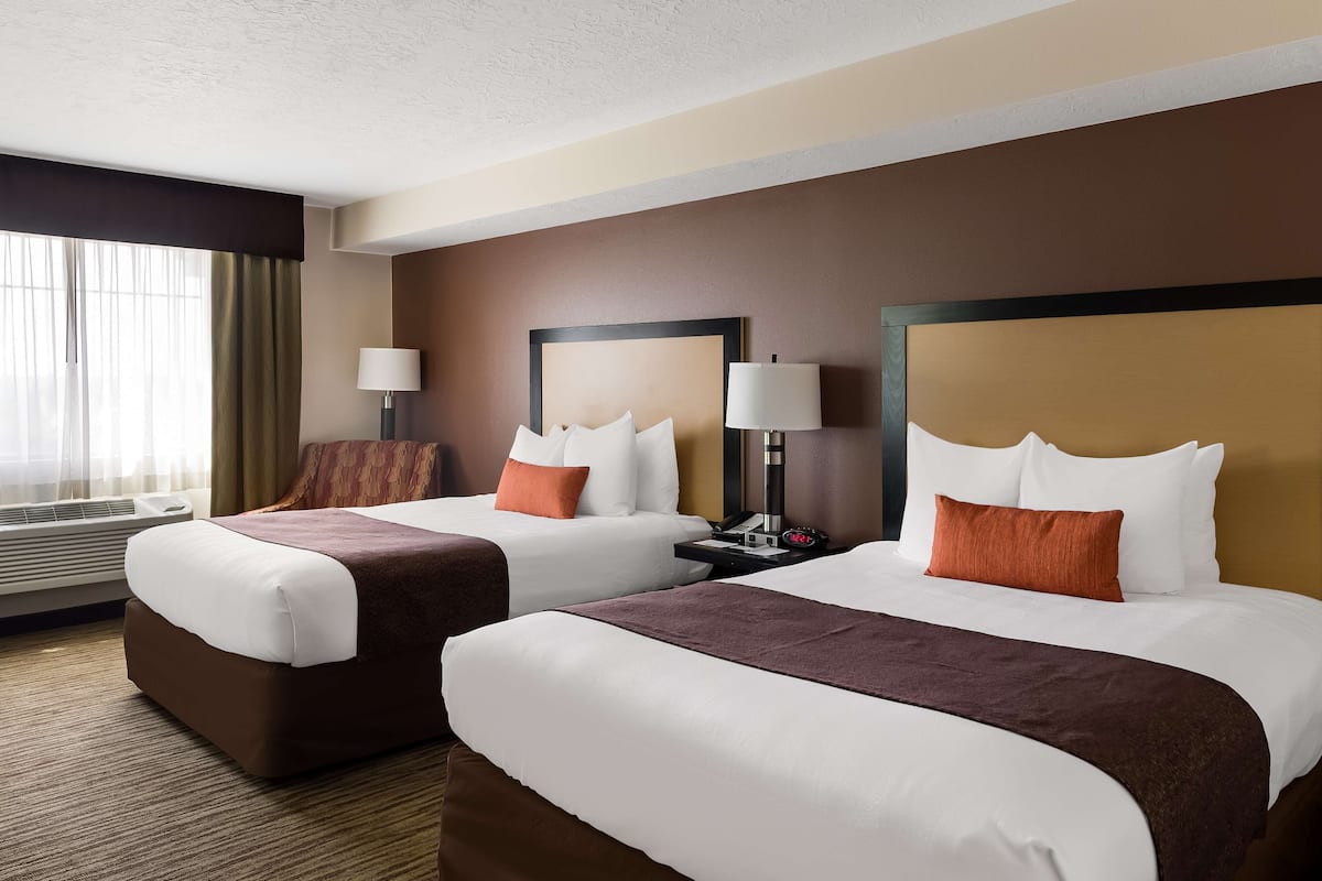 A hotel room with two beds, a nightstand with a lamp, and a large window with curtains.
