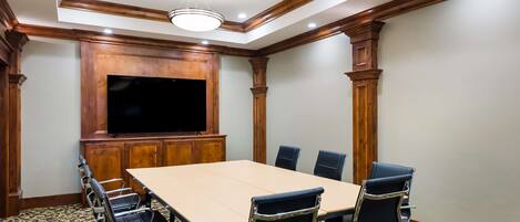 A conference room with a large table, six chairs, a flat-screen TV, wooden paneling, and patterned carpet.