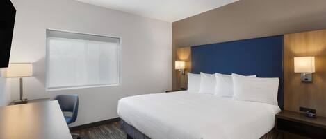 A hotel room with a large bed, a desk, a chair, and a window with blinds.