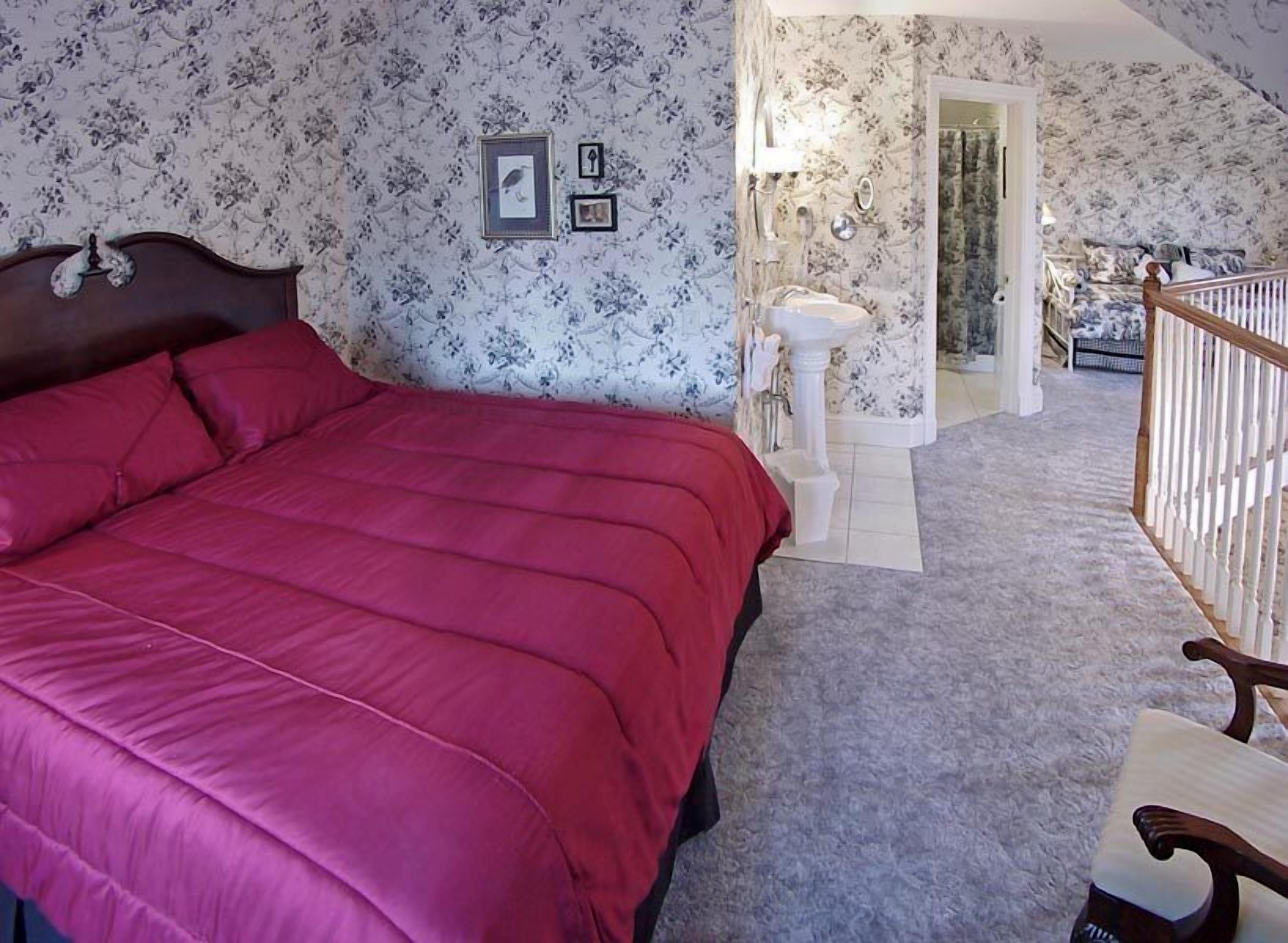 Ein Schlafzimmer mit einem großen Bett, einem hölzernen Kopfteil, einem weißen Waschtisch und einer Treppe, die in einen anderen Raum führt.