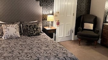A bedroom with a patterned bedspread, a nightstand with a lamp, a chair, and a wardrobe.
