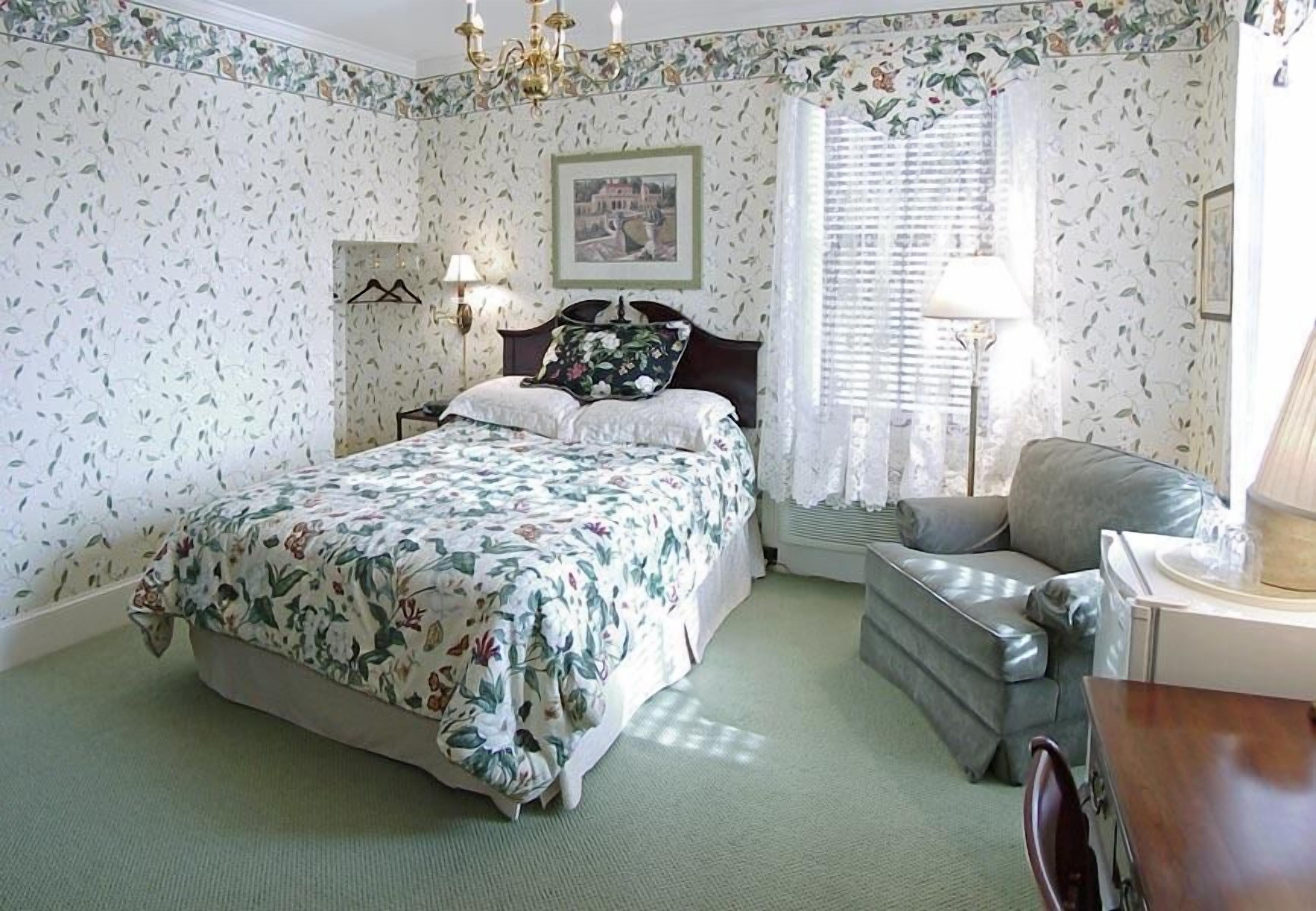 A bedroom with a floral-patterned bed, a grey sofa, a small table, and a picture on the wall.