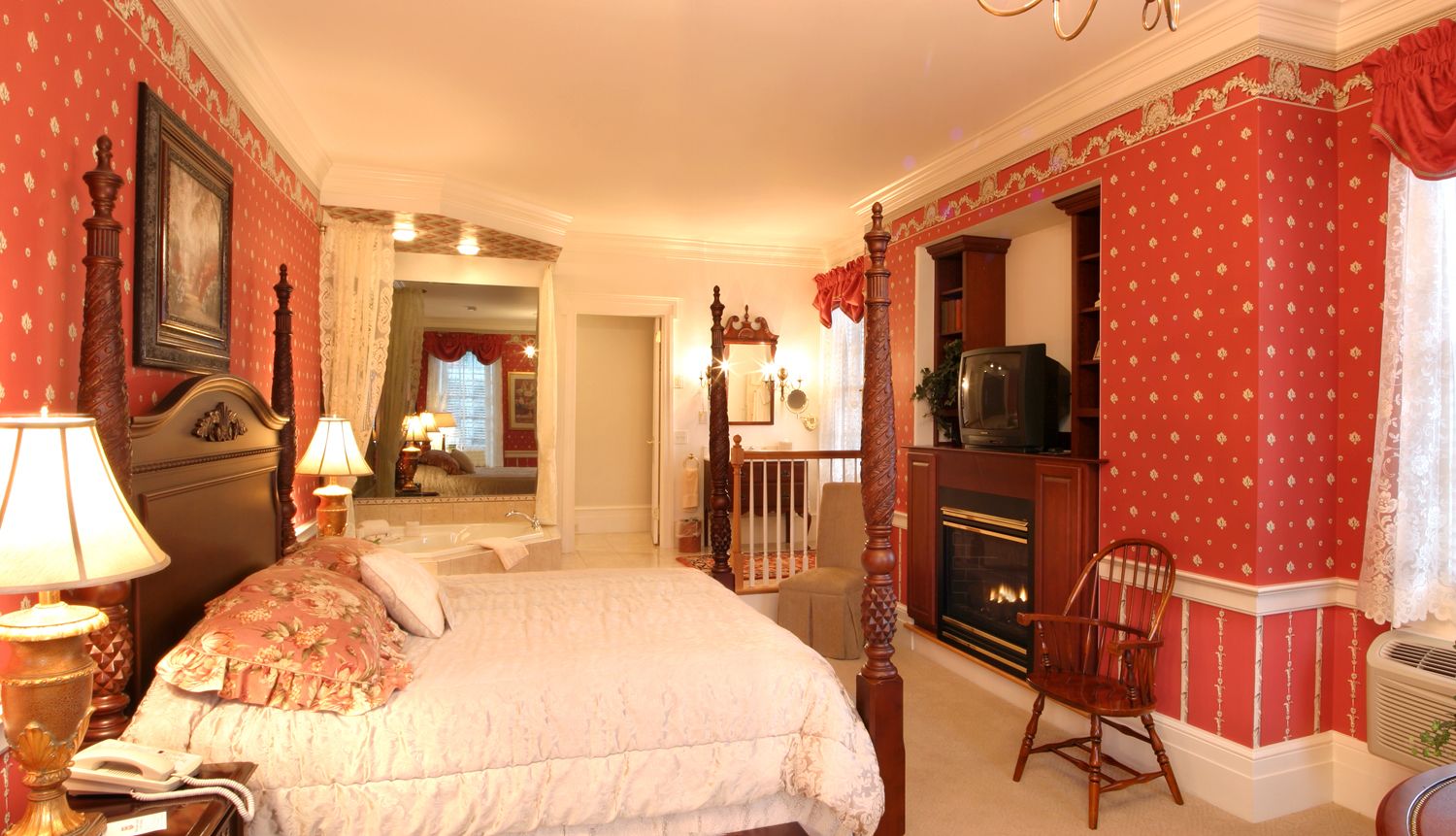 A bedroom with a large bed, a fireplace, a television, and a chair.
