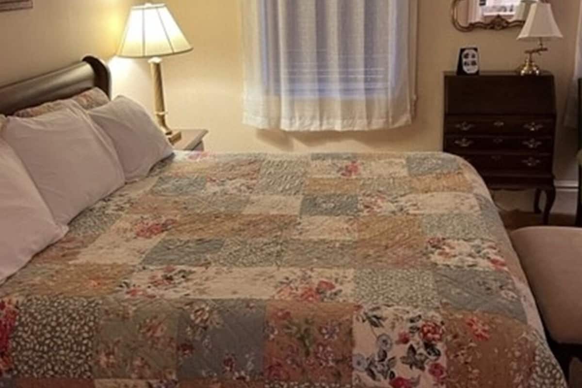 A bedroom with a bed, a nightstand, a dresser, a chair, and a window with curtains.