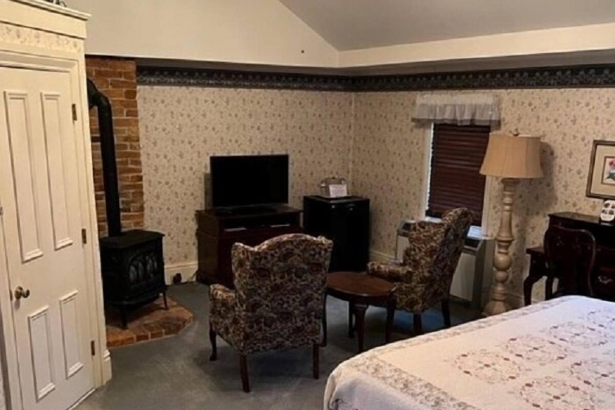 A bedroom with a bed, a television, a fireplace, and a ceiling fan.