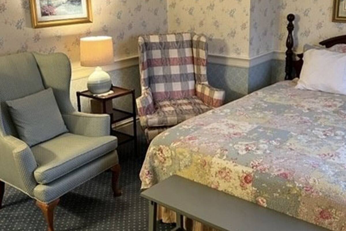 A bedroom with a bed, a chair, a nightstand, and a lamp.