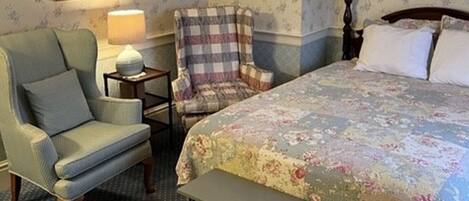 A bedroom with a bed, a chair, a nightstand, and a lamp.