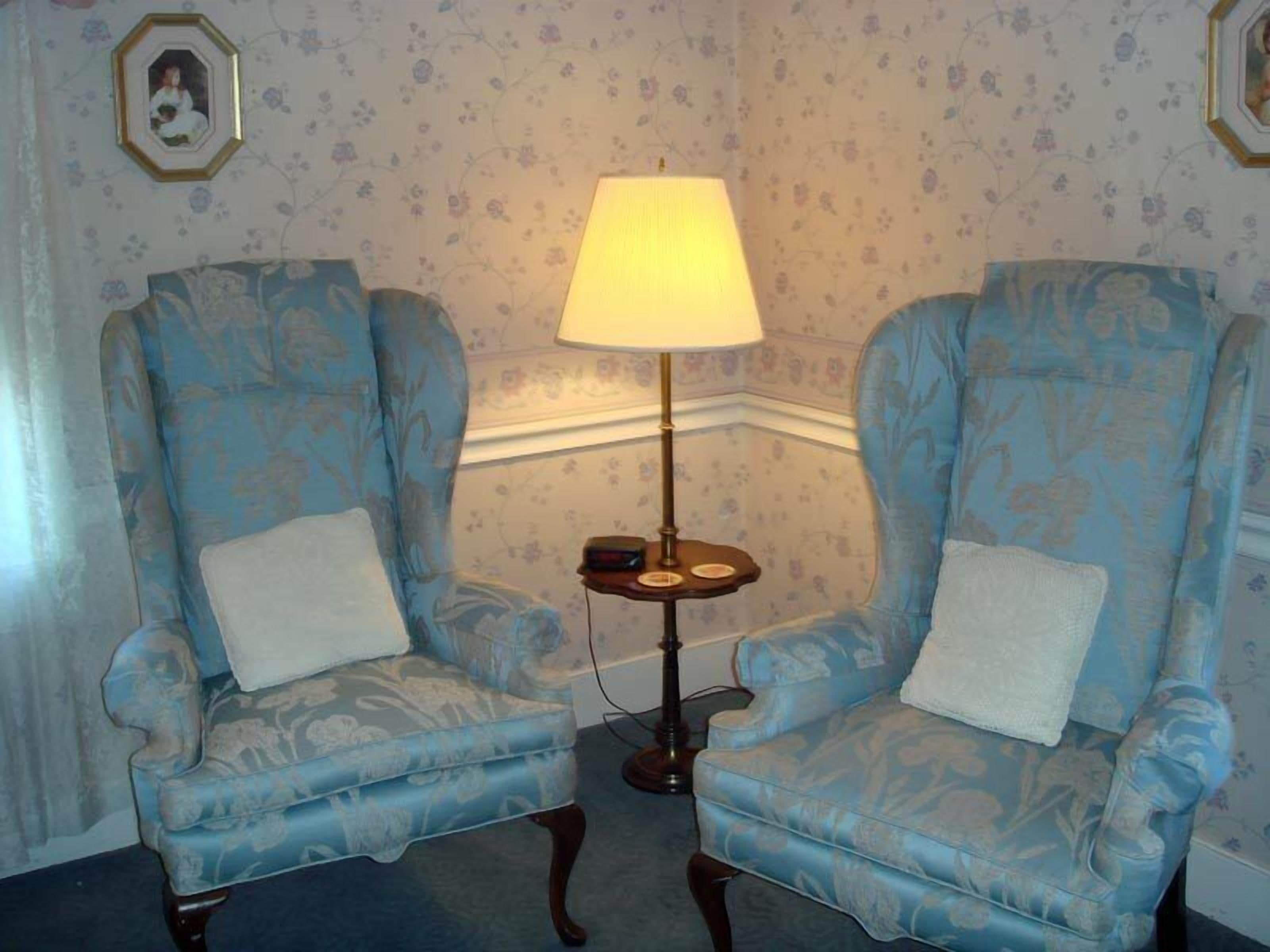 Two blue armchairs with white cushions, a floor lamp, and floral wallpaper.