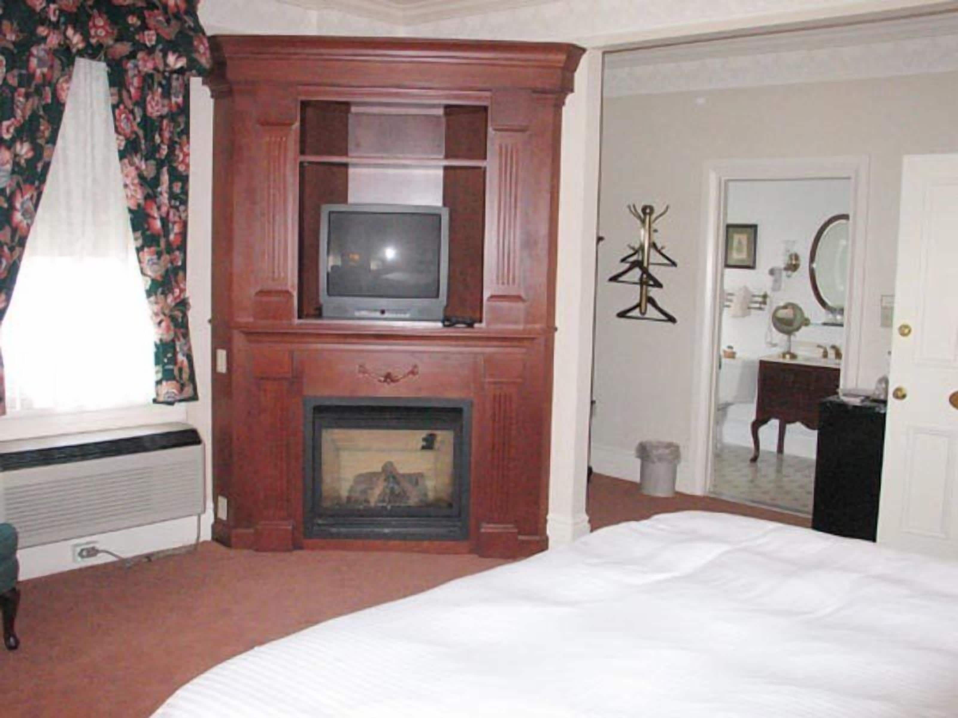 A bedroom with a fireplace, a television, a bed, and a door leading to a bathroom.