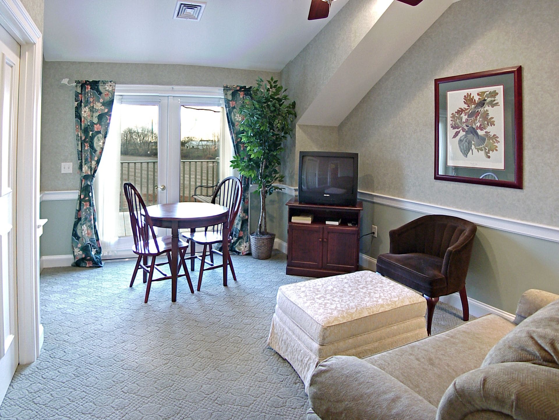 A living room with a dining table, chairs, a television on a stand, a sofa, and a framed picture on the wall.
