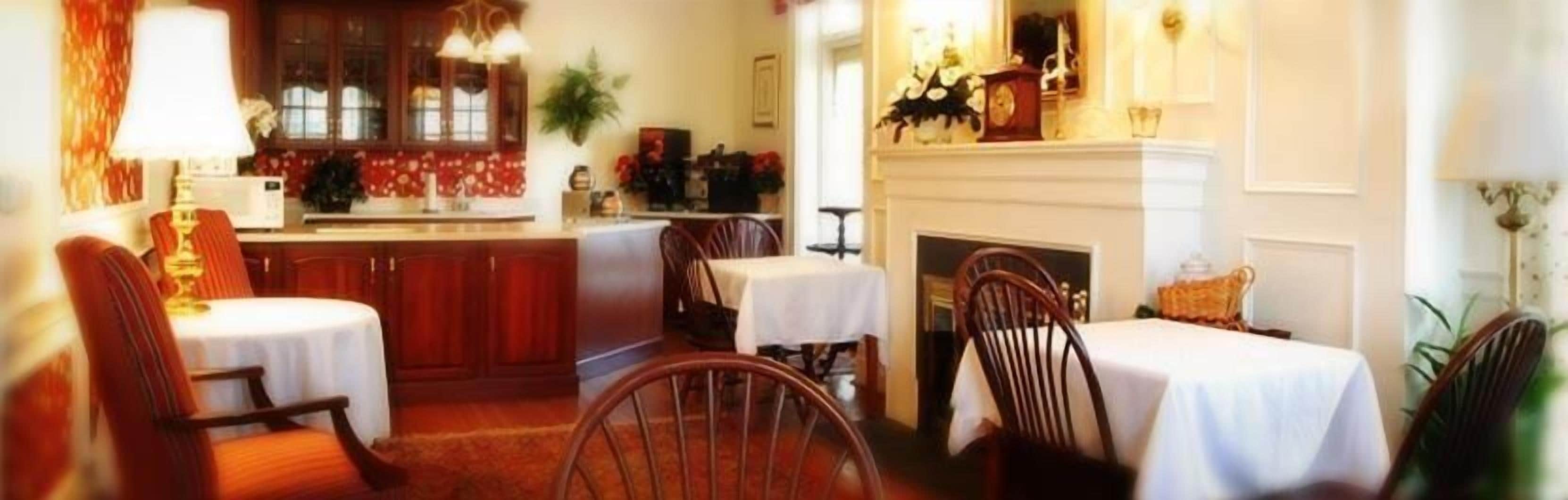 A dining area with wooden chairs and tables, a fireplace, and a kitchen area with cabinets and a stove.