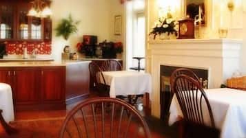 A dining area with wooden chairs and tables, a fireplace, and a kitchen area with cabinets and a stove.