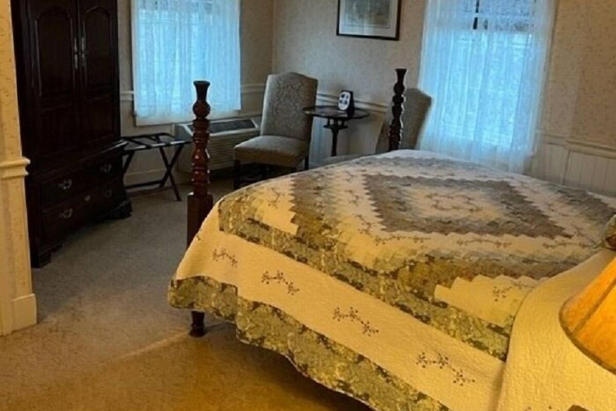 A bedroom with a large bed, a chair, a small table, and a cabinet.