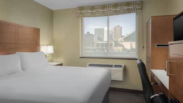 Habitación de hotel con una cama grande, un escritorio, una silla, un televisor y una ventana con vistas a edificios.