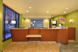 A reception desk with a wooden finish, a wall-mounted sign, and a window with blinds. - Holiday Inn Express New York - Manhattan West Side by IHG (New York)