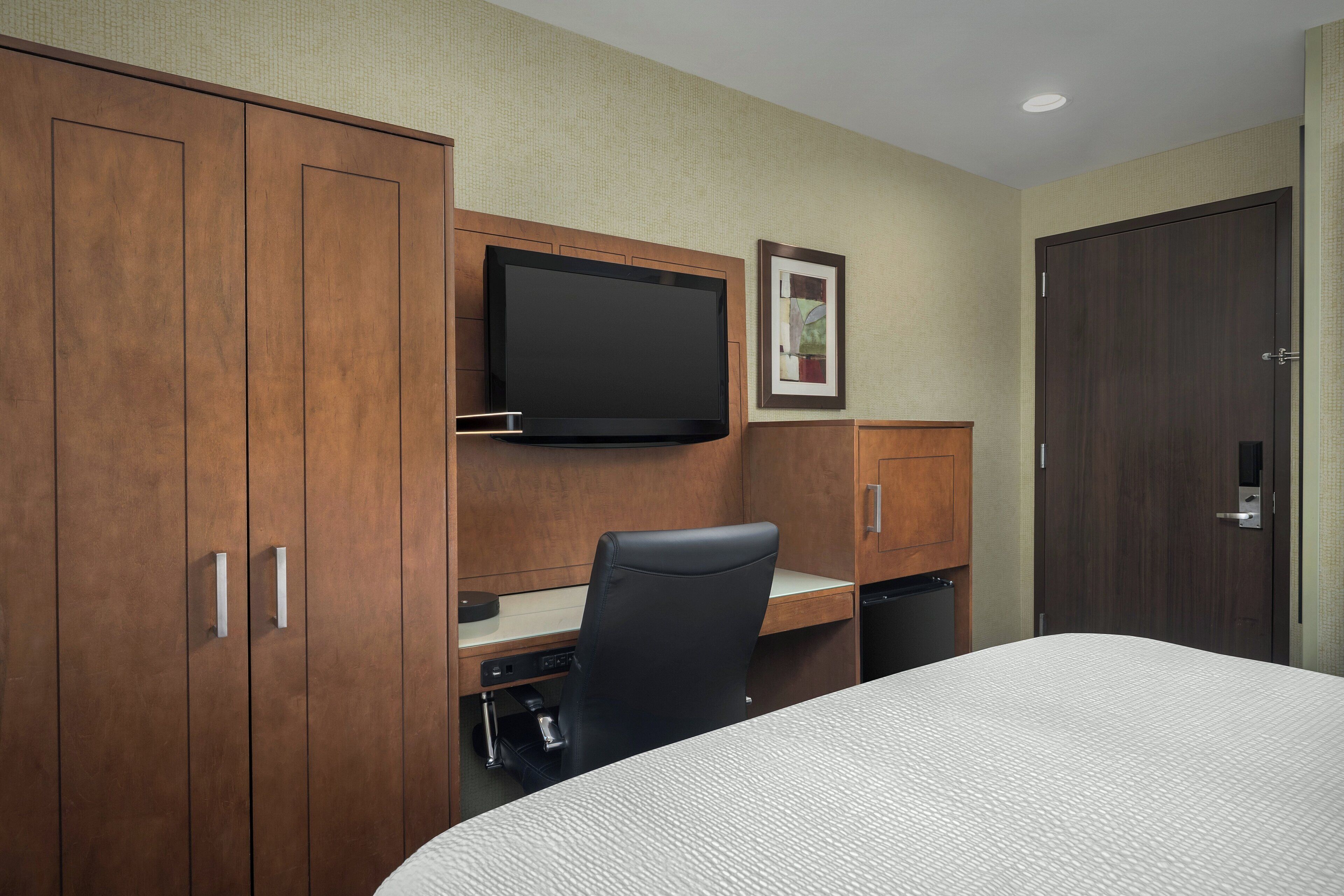 A hotel room with a bed, a desk with a chair, a television, and wooden wardrobes.