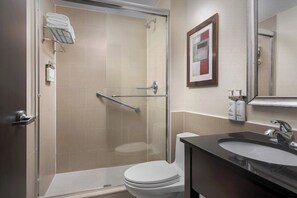 Un baño moderno con cabina de ducha de vidrio, inodoro blanco y lavabo oscuro con espejo.