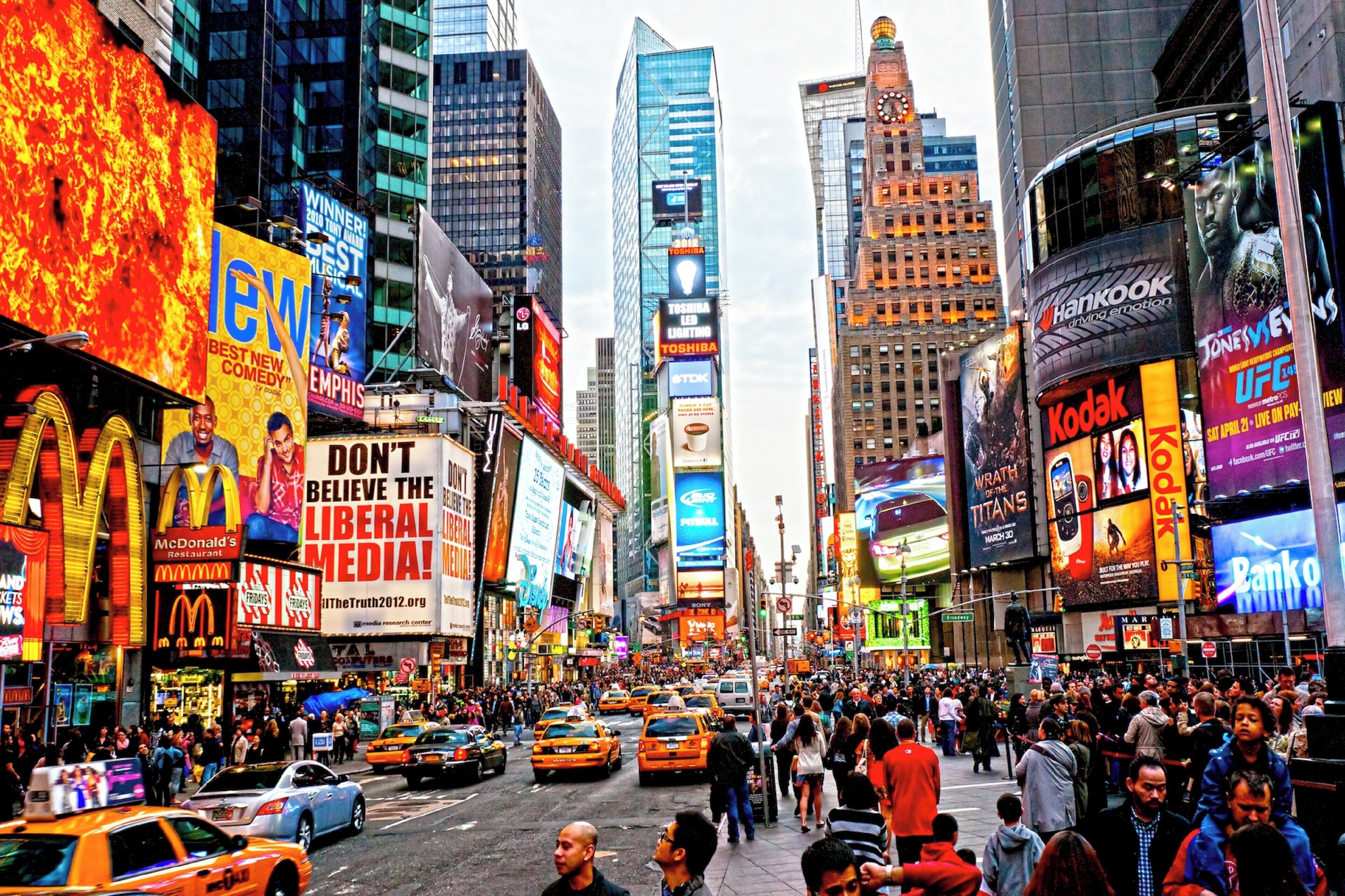 A busy urban street with tall buildings, billboards, and a crowd of people.