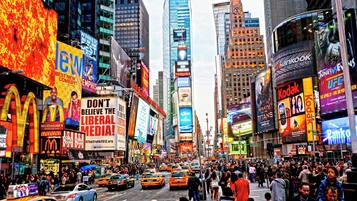 A busy urban street with tall buildings, billboards, and a crowd of people.