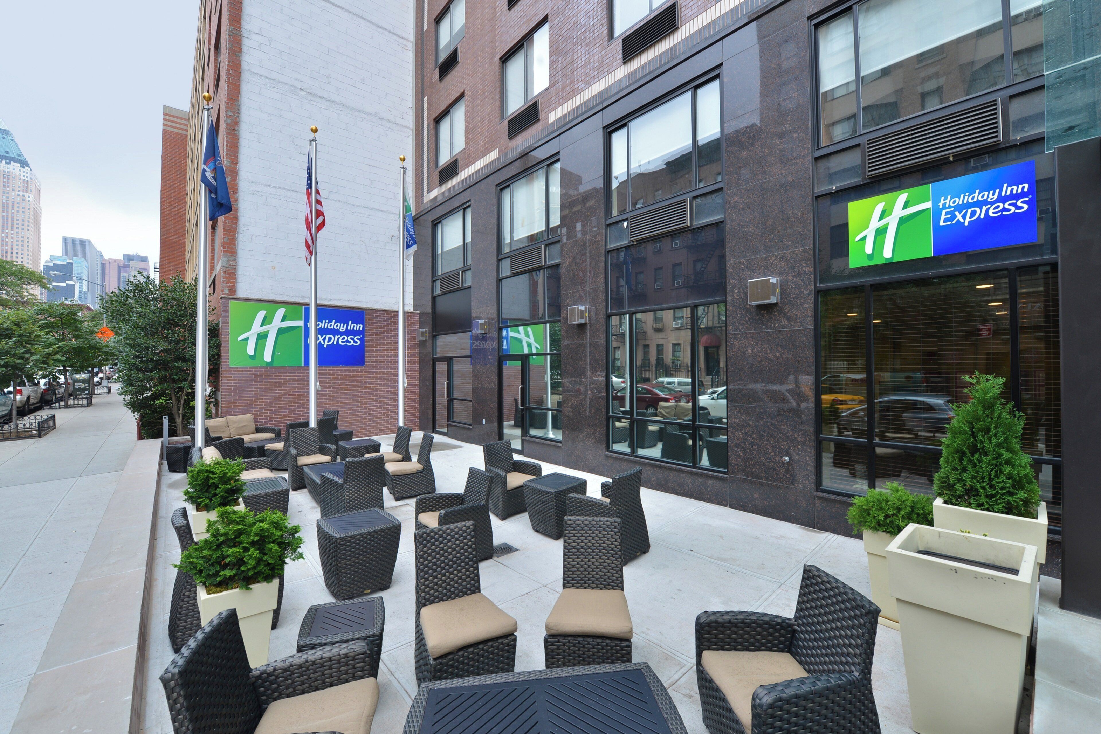 An outdoor seating area with wicker furniture and potted plants, a Holiday Inn Express sign, and a brick building facade.
