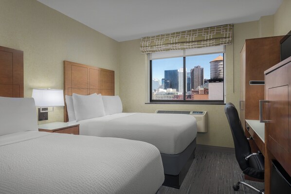Una habitación de hotel con dos camas, un escritorio, una silla y una ventana con vista a la ciudad.