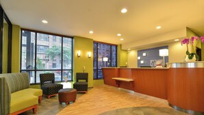 A lobby with a reception desk, seating area with chairs and a sofa, large windows with blinds, and a wooden floor. - Holiday Inn Express New York - Manhattan West Side by IHG (New York)