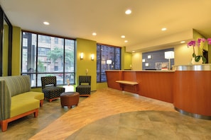 A lobby with a reception desk, seating area with chairs and a sofa, large windows with blinds, and a wooden floor. - Holiday Inn Express New York - Manhattan West Side by IHG (New York)