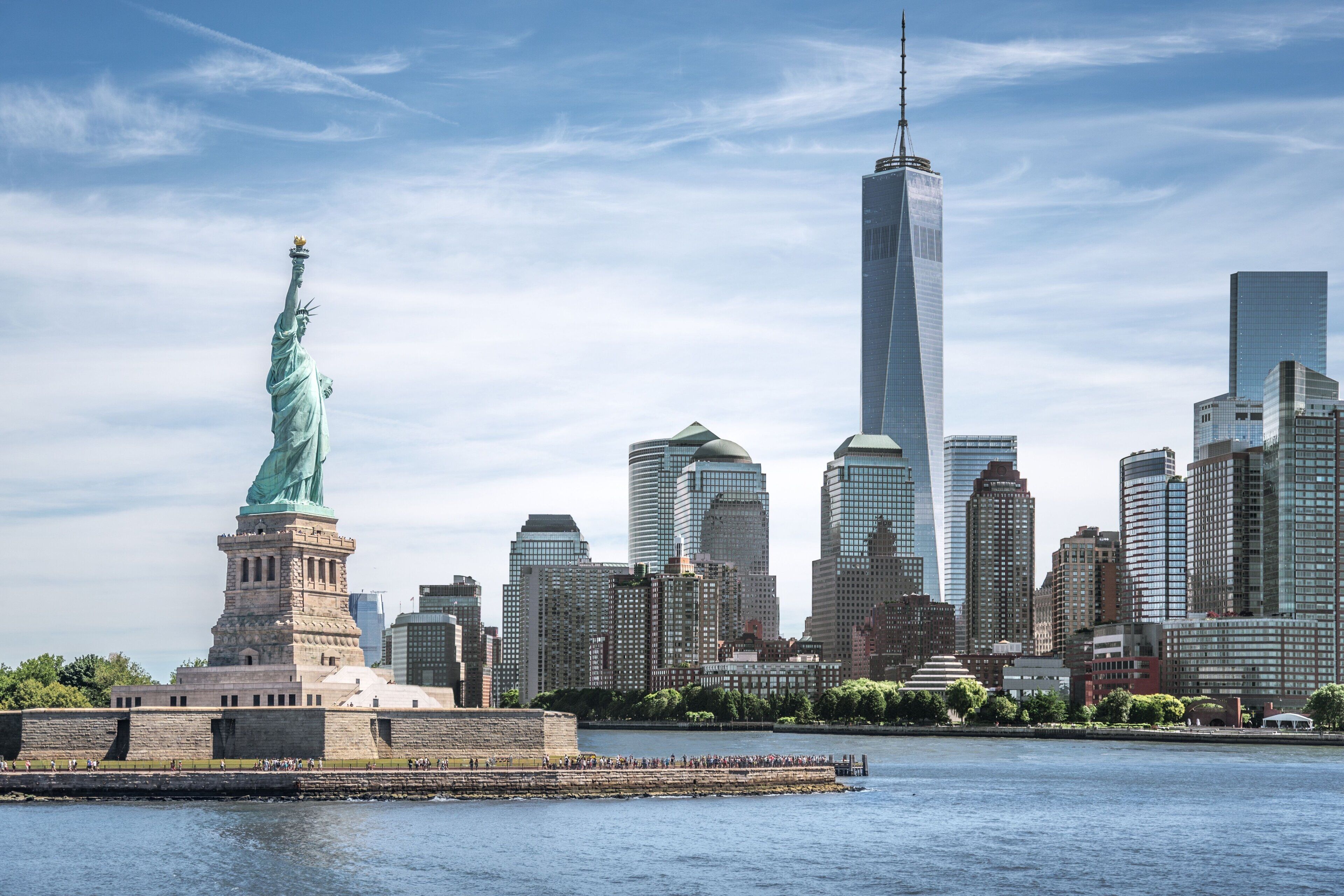 The Statue of Liberty in front of a city skyline with modern skyscrapers.