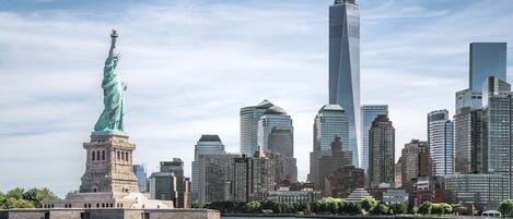 La Estatua de la Libertad frente a un horizonte urbano con rascacielos modernos.