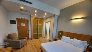 A hotel room with a large bed, a sofa, a small table, a nightstand, and a wardrobe with a sliding door. - La Boroña (Gijon)