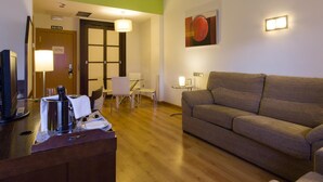 A hotel room with a wooden floor, a sofa, a desk with a coffee machine, a TV, and a door labeled "SALIDA". - La Boroña (Gijon)