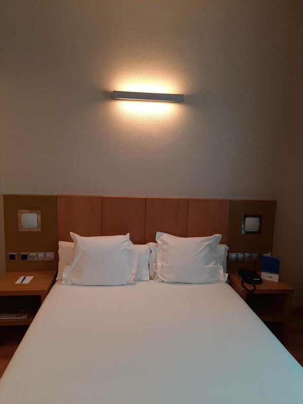 A hotel room with a large bed, two bedside tables, a wall-mounted light, and a wooden headboard. - La Boroña (Gijon)