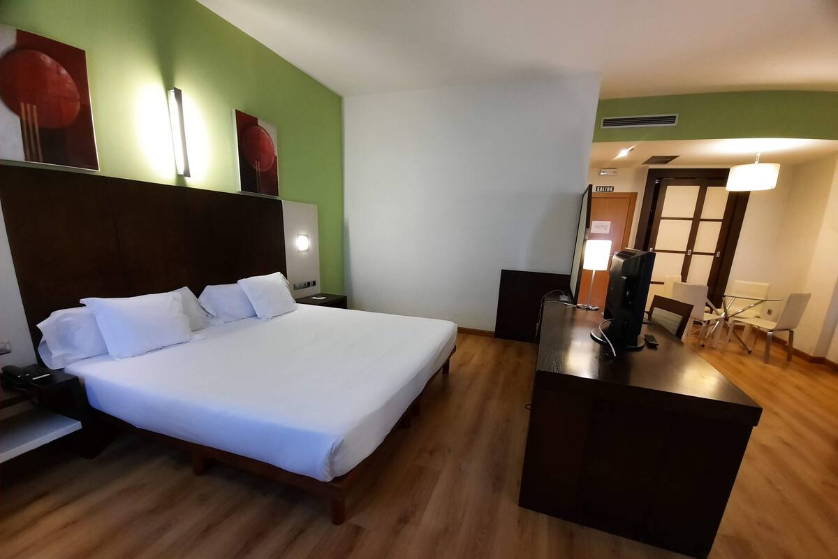 A hotel room with a large bed, a desk with a computer, and a seating area with chairs.