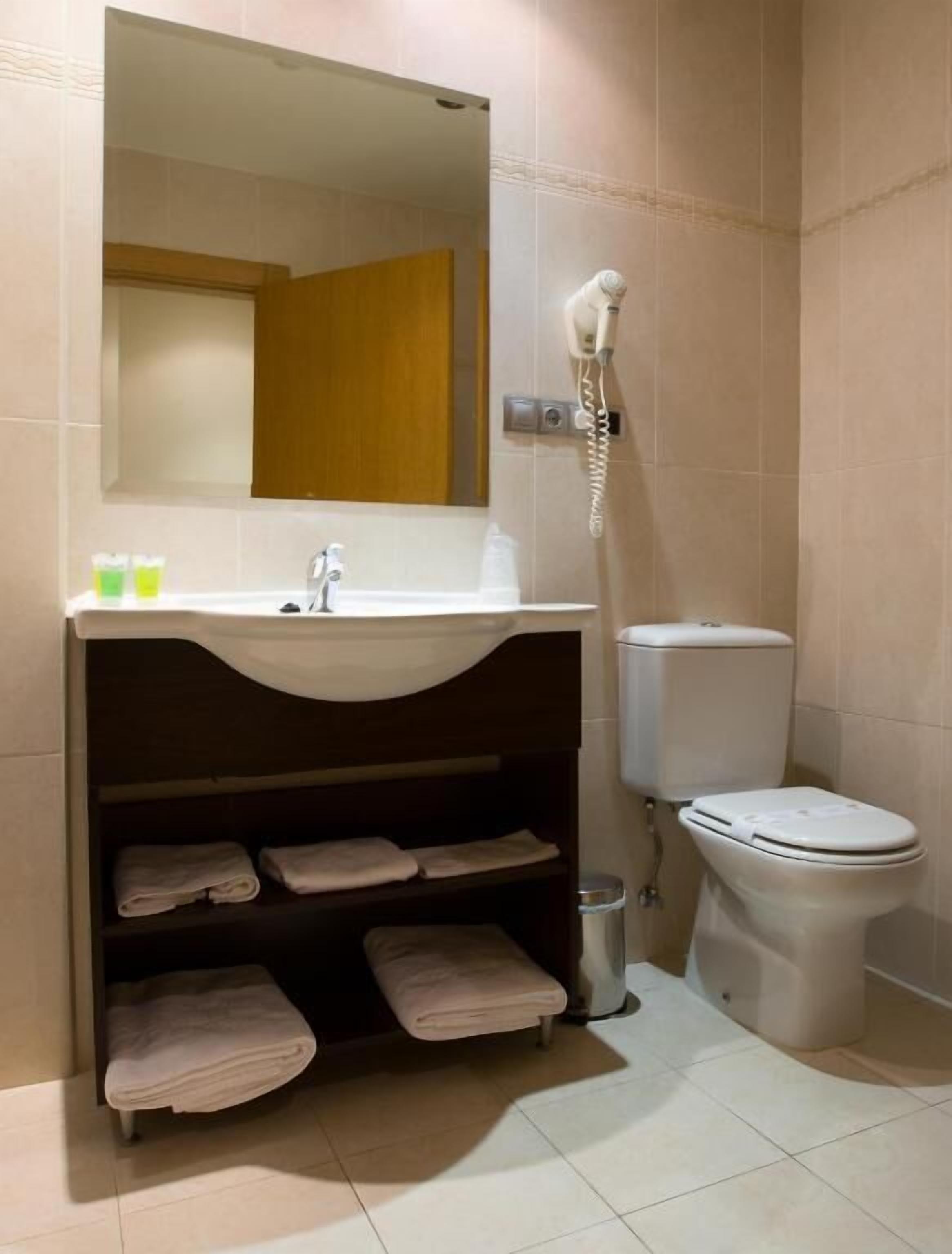 A bathroom with a sink, mirror, towel rack, toilet, and a hairdryer.