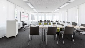 Een vergaderzaal met een grote tafel, meerdere stoelen, een whiteboard en een presentatiescherm.