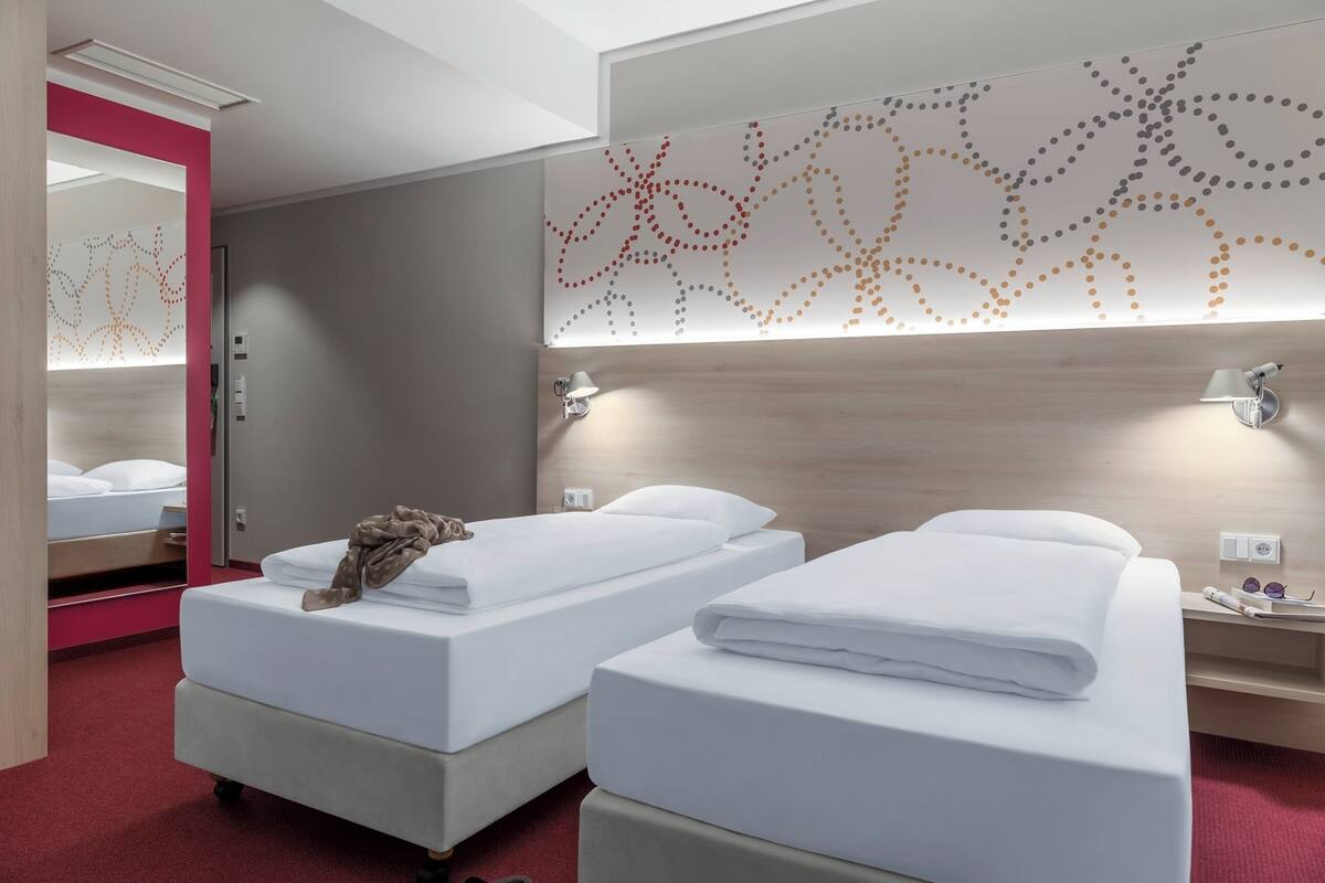 Een hotelkamer met twee bedden, een spiegel, een kunstwerk aan de muur en een nachtkastje met een lamp.