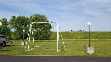 Enjoy a serene escape in this peaceful outdoor space with a swing set and a lamp post, surrounded by a lush grassy field and trees.