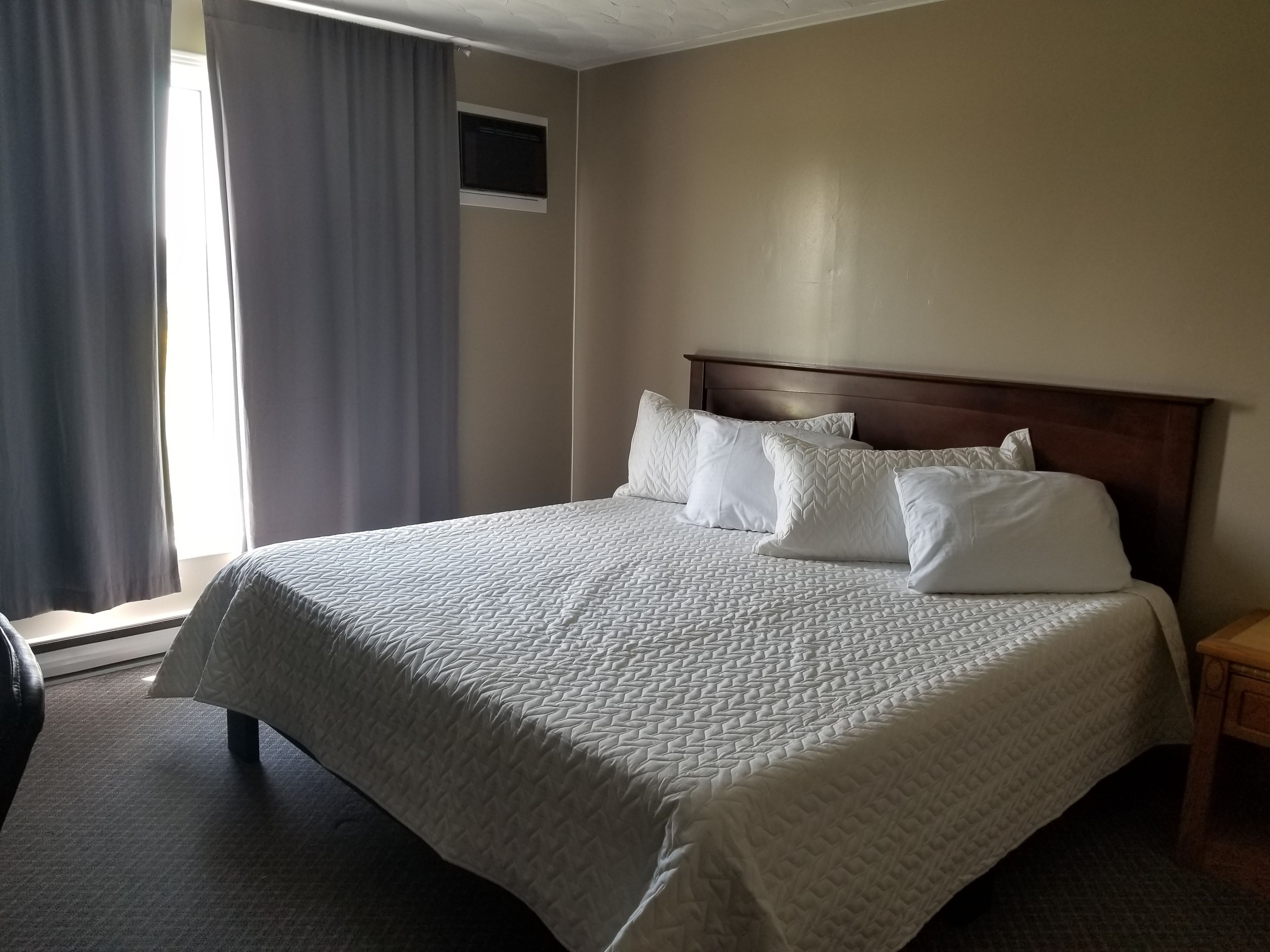 A hotel room with a large bed, a wooden headboard, and a small bedside table.