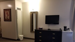 A hotel room with a black dresser, a mirror, a television, and a coffee maker. - Knights Inn Woodstock (Jacksonville)